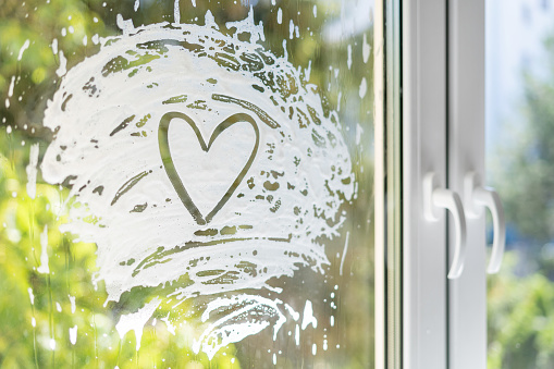 heart shape soap foam on window glass with view of green trees against blurred background. cleaning service concept. advertising pf organic and eco friendly detergent