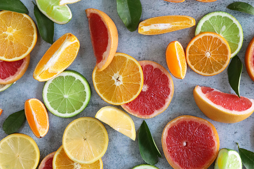 Stock photo showing citrus fruit wedges and slices on mottled grey background, modern minimalist photo of circular sliced oranges, lemon and lime citrus fruits showing segments, seeds / pips and rind around edge, healthy eating concept photo for vitamin C and fruit juice.