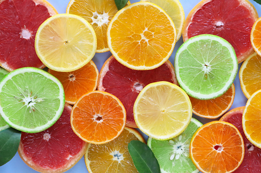 Stock photo showing layers of citrus fruit slices on blue background, modern minimalist photo of circular sliced oranges, lemon and lime citrus fruits showing segments, seeds / pips and rind around edge, healthy eating concept photo for vitamin C and fruit juice.