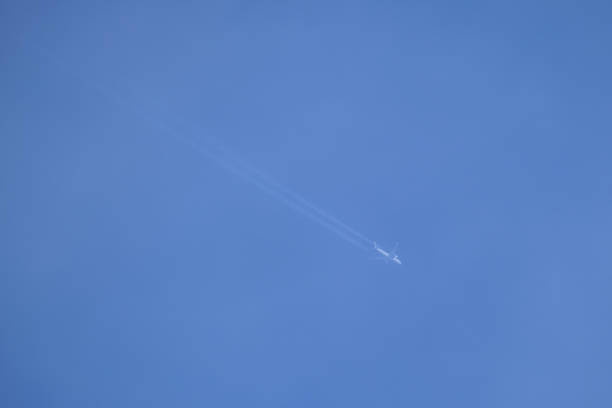 istock Distant passenger jet plane flying on high altitude on clear blue sky leaving white smoke trace of contrail behind. Air transportation concept 1422876337