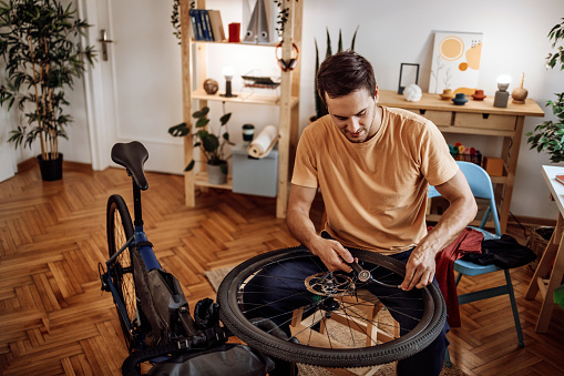 Young casually clothed man inflating bicycle tire in his apartment