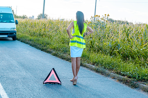 A Woman had a Traffic Accident on a Road and She is Putting a Warning Sign on the Ground.