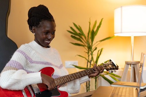 Young woman giving or receiving online electric guitar classes with her laptop