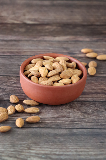 Stock photo showing close-up view of some almonds that are piled high in a brown dish, against a woodgrain background. Raw almonds are considered to be a very healthy snack food, containing vitamin E, antioxidants and protein, and boasting a list of health benefits while aiding blood sugar control.