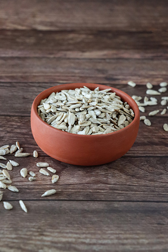 Stock photo showing close-up view of some white sunflower seeds piled high in a brown dish, against a woodgrain background. Raw sunflower seeds are considered to be a very healthy snack food and are high in vitamin E, selenium, antioxidants and protein, boasting a list of health benefits and may aid lower blood pressure.