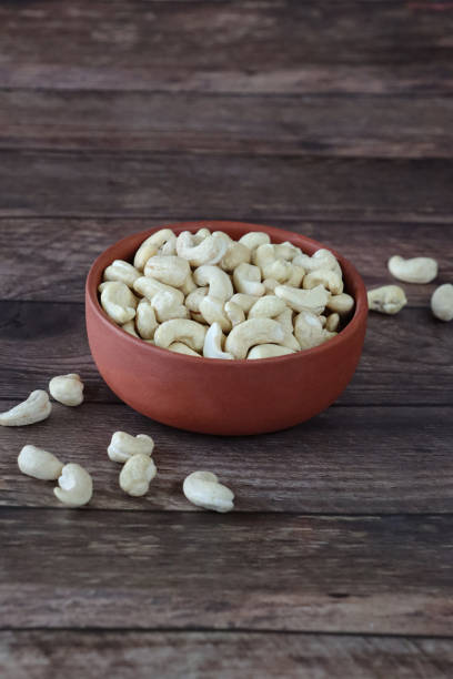 Close-up image of pile of cashews in brown bowl, healthy food snack, wood grain background, focus on foreground, copy space stock photo