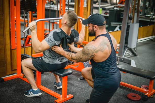 istock Man doing exercises in the gym with a man trainer athletic physique 1422882307