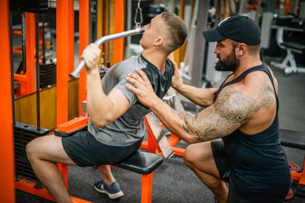 istock Man doing exercises in the gym with a man trainer athletic physique 1422882581