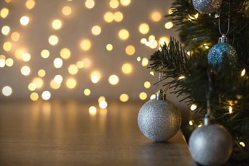 Decorated Christmas tree with silver and blue glittering balls against orange glittering blurred lights, an empty space on a brown wooden table, close-up