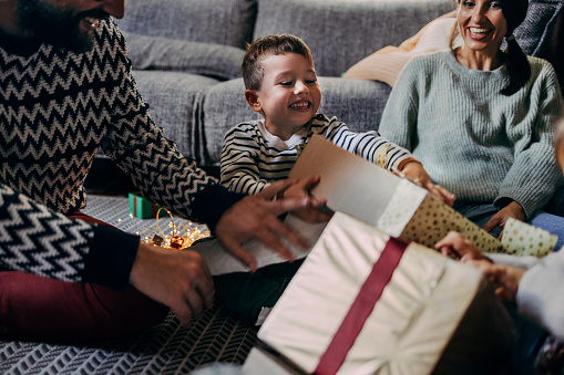 Smiling boy opening Christmas presents with his family.