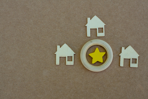 Outlines of three houses with placed left, right and above a wooden circle with a yellow wooden star inside, on brown backdrop, with copy space.