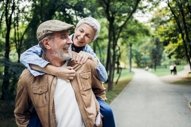 Happy senior man carrying his wife and having fun in the park stock photo