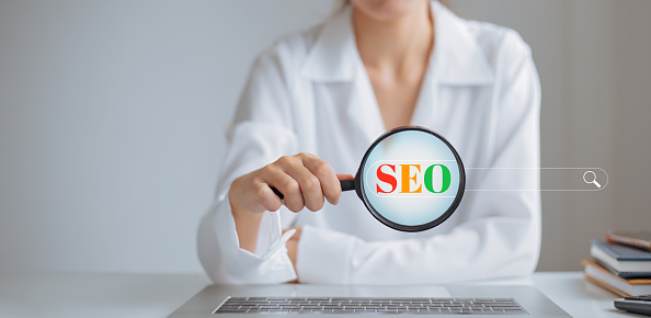 Female hand holding a magnifying glass to magnify SEO letters on the search bar.