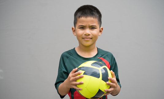 Kid holding soccer ball with grey backdrop in the background.