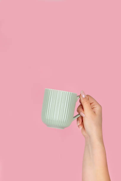 istock Arms raised up holding coffee cup on pink background. 1422948213