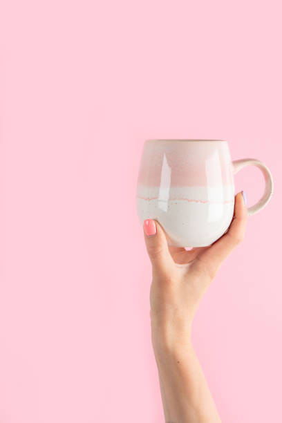 istock Arms raised up holding coffee cup on pink background. 1422948228