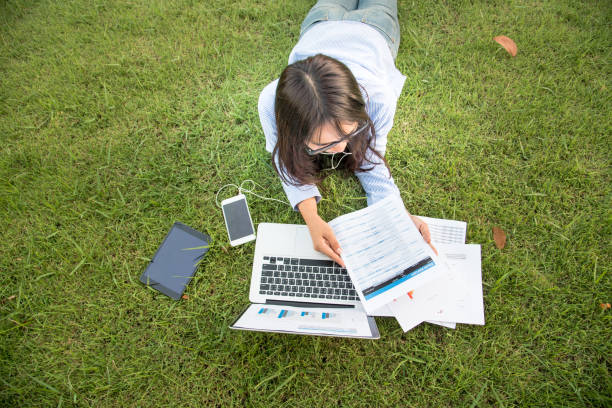 Asian woman lay down green garden park using laptop working outdoor home office. Happiness Woman smile working Freelance on laptop. Young Women University student type computer laptop at green nature stock photo