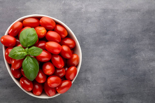 Fresh tomatoes in bowl on pastel table. Tomato background, healthy vegetables and basil leaves.
