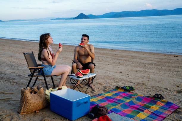 Millennial-aged couple eating watermelon at the beach while on vacation in Japan