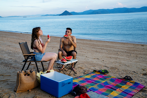 Millennial-aged couple eating watermelon at the beach while on vacation in Japan