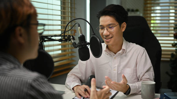 istock Smiling man host interviewing guest while recording live podcast in home studio. Radio, podcasts and technology concept. 1422975518