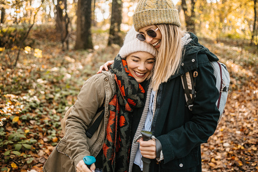 Two young women hugging while hiking in a forest. Spending time with friends and having fun