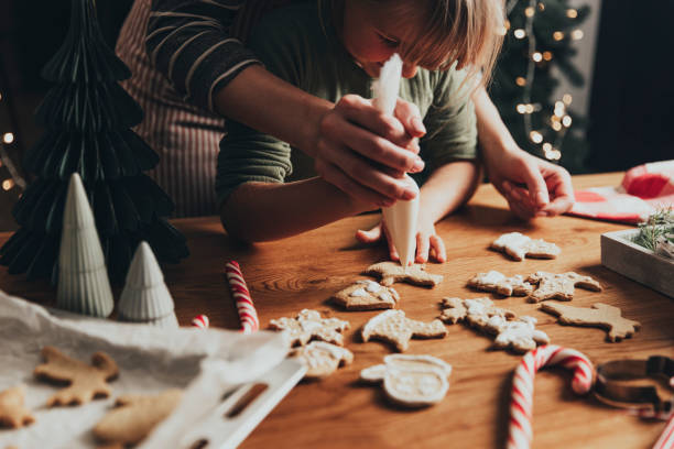 Christmas, New Year food preparation. Gingerbread cookies decorating with icing Christmas and New Year food preparation. Xmas gingerbread cooking and decorating freshly baked cookies with icing and mastic. Mom helping cute little daughter to decorate cookie on wooden messy table cake models stock pictures, royalty-free photos & images