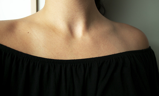 A close-up of the shoulders and clavicles of a young woman, wearing a black, offshoulder t-shirt.