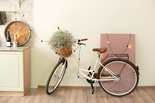 Stylish interior of light spacious room with modern bicycle and lights garland. Interior of modern room with big picture and retro bicycle for hipster. Bicycle parked decorate interior living room