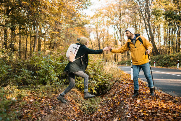 Hiker helping his girlfriend to jump over a ditch