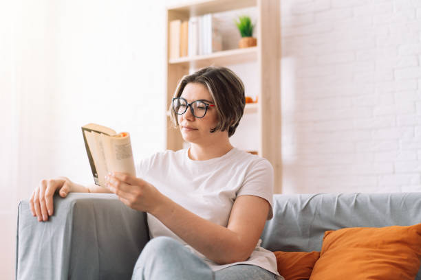 istock Girl with glasses reading book on the couch 1422982973