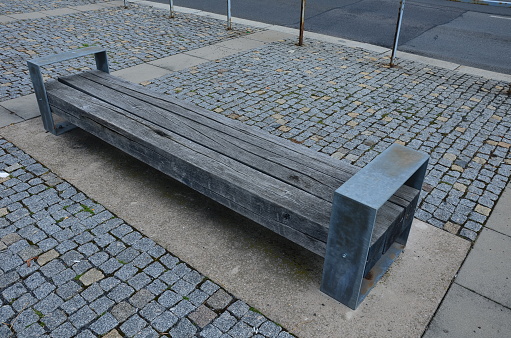 Wooden public bench with a stone wall behind.