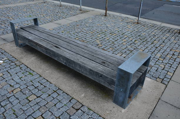 wooden long bench, where the seating area is formed by rows of vertical planks and a backrest. notches are possible on the edges of the bench for inserting a bicycle tire. park with perennials wooden long bench, where the seating area is formed by rows of vertical planks and a backrest. notches are possible on the edges of the bench for inserting a bicycle tire. park with perennials backrest stock pictures, royalty-free photos & images