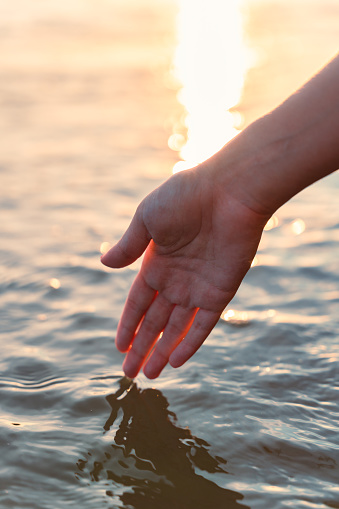 Hand of woman touching the water surface during the sunset