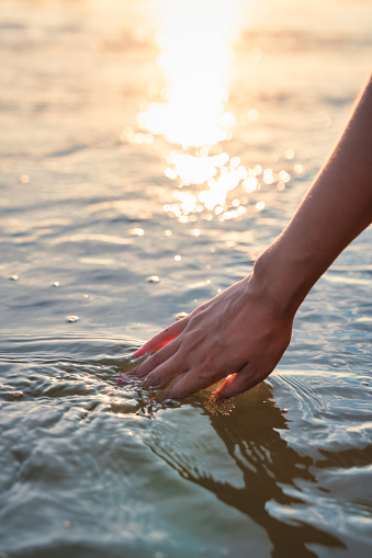Hand of woman touching the water surface during the sunset
