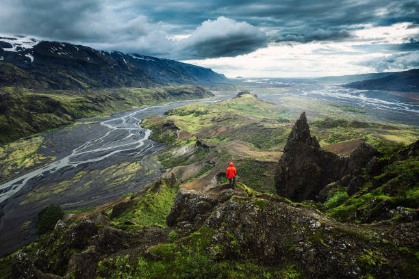Hiker man in red jacket standing on top of Valahnukur surrounded by volcanic mountain and Krossa river in Icelandic Highlands at Thorsmork stock photo