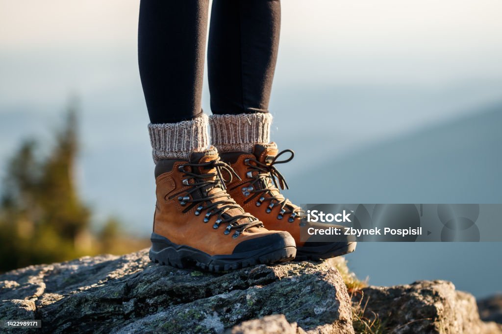 Leather hiking boots in mountain peak Hiking boot. Female legs with leather ankle shoes and knitted wool socks on mountain peak during trekking outdoors Hiking Boot Stock Photo