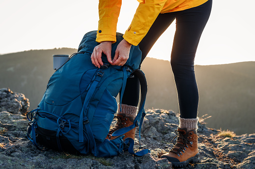 Woman opening backpack after climbing mountain peak. Hiking outdoors. Female tourist unpacking rucksack