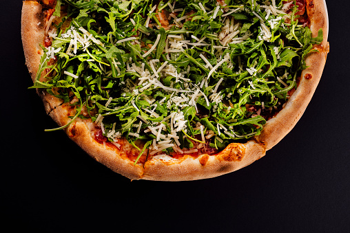Pizza with arugula and parmesan on black