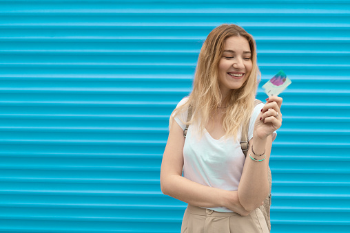 Portrait of a beautiful young woman in front of the blue background, holding a credit card