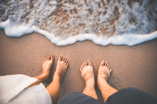 Closeup traveler man and woman foot of relax on beach with sea wave in summer, Holiday travel vacation concept