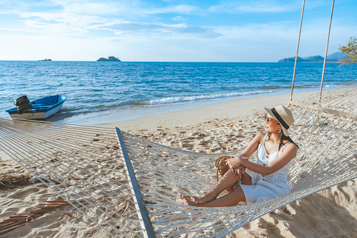 Summer travel vacation concept, Happy traveler asian woman with hat relax in hammock on beach in Koh Chang, Trad, Thailand