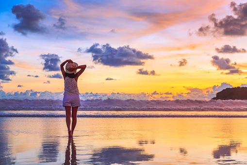 Summer travel vacation concept, Traveler asian woman with hat relax and sightseeing on Kata beach at sunset in Phuket, Thailand