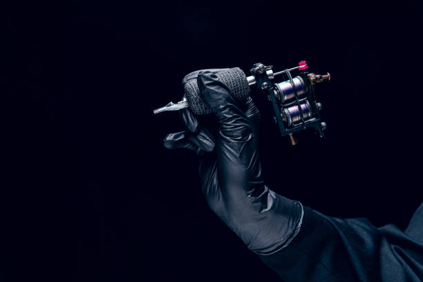 istock Machine for tattoo. Human hand in black protective glove holding professional equipment for making tattoo on body isolated on dark background. 1423002981