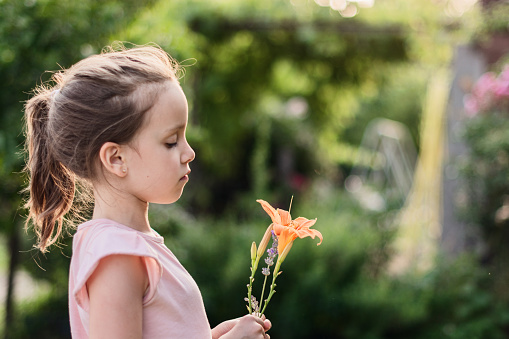 Side view of little girl holding lily flower during spring day in the yard