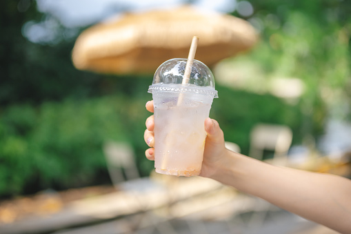 Hand holding Fruit juice in recycleable Plastic juice cup with recycle paper straw sustain green nature background outdoor