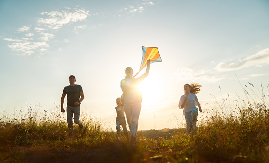 Happy family running through field with kite.