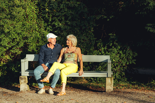 Senior couple sitting on a bench in the park and looking at each other. Wealthy couple spending time together at park on a weekend.