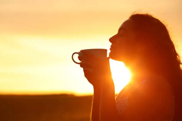 Photo of Silhouette of a woman smelling coffee at sunset