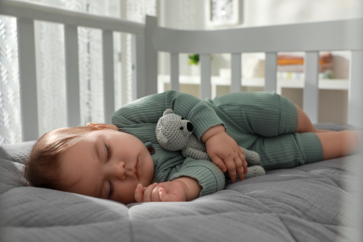 A little baby is sleeping in his crib next to the parents' bed. He’s sucking his thumb.